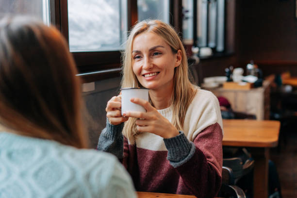 portrait of an attractive blonde chatting with a friend while sitting in a cozy warm cafe. - apres ski winter friendship ski imagens e fotografias de stock