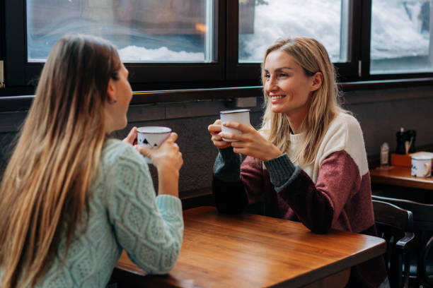 dos mujeres jóvenes y bonitas están hablando en un bar tomando un café. - apres ski friendship skiing enjoyment fotografías e imágenes de stock