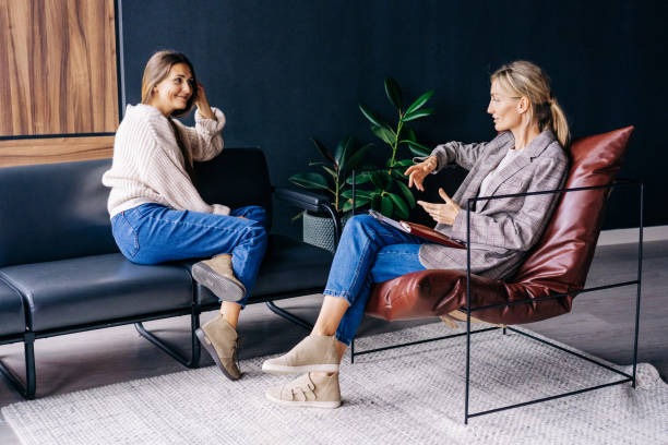 A smiling woman listens to the advice of a consultant psychologist sitting on a sofa in the workshop A smiling woman listens to the advice of a consultant psychologist sitting on a sofa in the workshop. counseling stock pictures, royalty-free photos & images