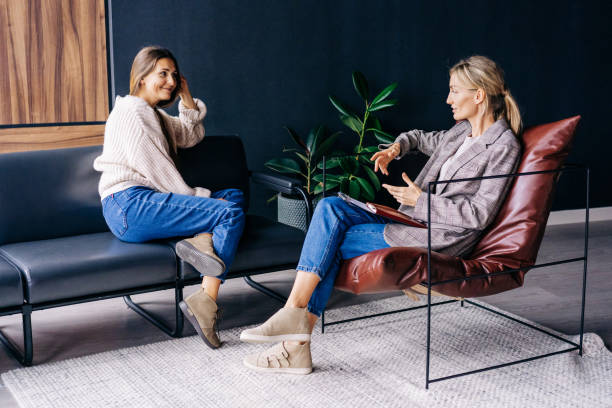 A smiling woman listens to the advice of a consultant psychologist sitting on a sofa in the workshop A smiling woman listens to the advice of a consultant psychologist sitting on a sofa in the workshop. mental health professional stock pictures, royalty-free photos & images