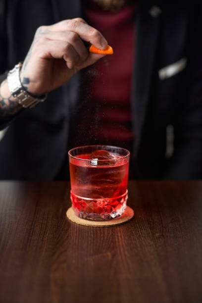istock Bartender prepairing a cocktail at the bar, squeezing an orange peel over a drink in a cocktail on an old-fashioned glass 1369379137