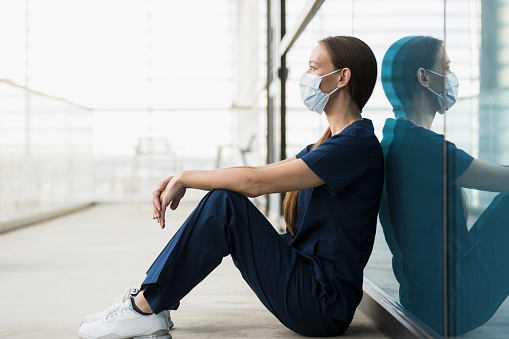 Sitting on the floor still wearing her protective mask, the operating room nurse takes a quick break.