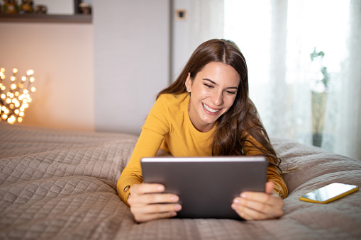 happy smiling woman, using a digital tablet at home, laying down in the bedroom
