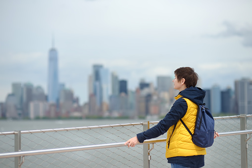 Woman tourist is admiring of famous panorama of Manhattan from island of Liberty. Sightseeing of New York, USA.