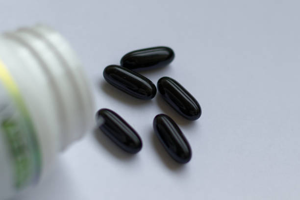 черные таблетки, выплескивающиеся из белого флакона - vitamin a vitamin b complex pill bottle medicine стоковые фото и изображения