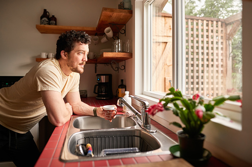 Young man in pajamas leaning on a kitchen counter in the morning and drinking a cup of coffee