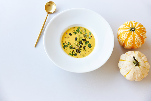 Various photos of a pumpkin soup in a white plate decorated with pumpkins and a golden spoon