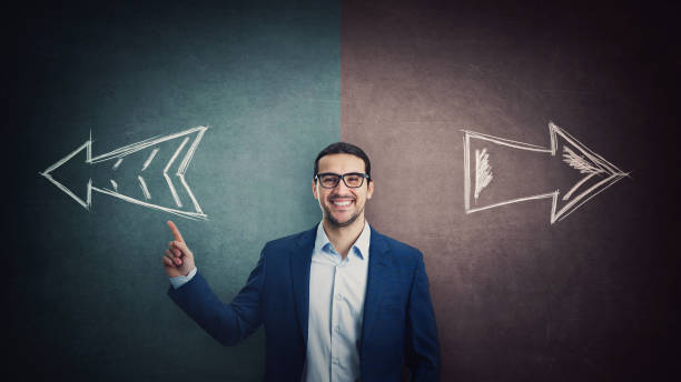 istock Confident businessman pointing forefinger choosing the correct direction. Determined man select an option in front of a split wall with arrows showing two different routes. Business choice concept 1369393571
