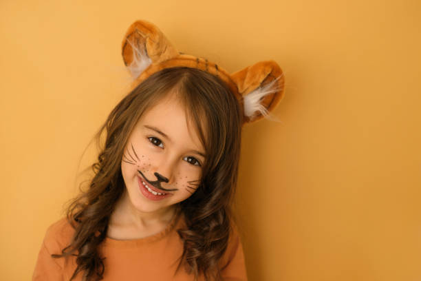 Girl with a tiger mask pattern on her face and a headdress with ears A nice smiling girl with a tiger mask pattern on her face and a headdress with ears looks sweetly into the camera. Stage makeup on a child's face cat face paint stock pictures, royalty-free photos & images