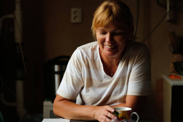 desenfoca a la joven mujer caucásica feliz que sonríe mientras está sentada en casa con una taza de café o té. rutina matutina en cocina. estilo de vida en el hogar. feliz mujer de 40 años en casa. fuera de foco - 40 45 years fotos fotografías e imágenes de stock