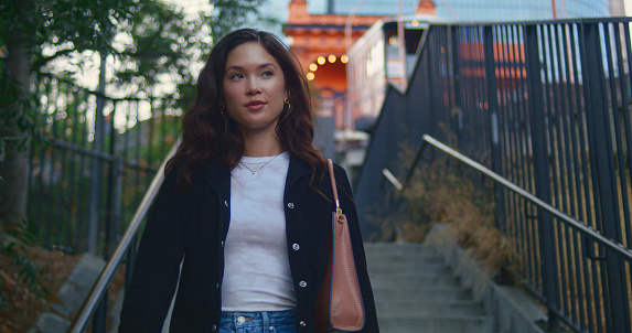 Cute happy girl walk down stairs city park. Confident asian woman going on ladder outdoors close up. Pretty brunette female move down stairway modern town. Active town life on summer weekend.