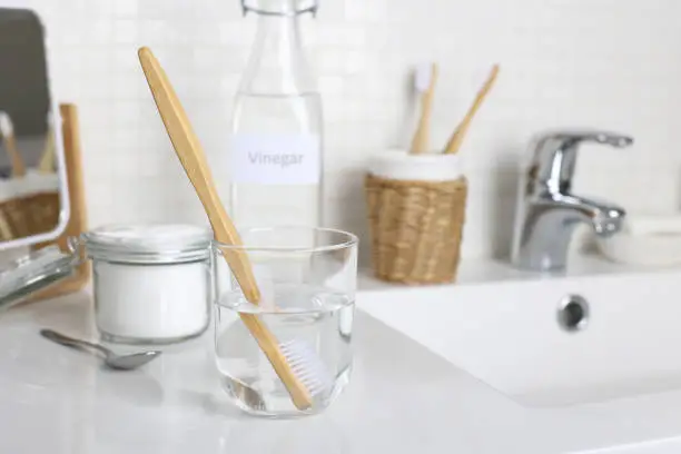 A toothbrush soak in a solution of  white vinegar, water and baking soda solution on  the bathroom sink. Natural desinfection. Hygiene and healthy lifestyle.
