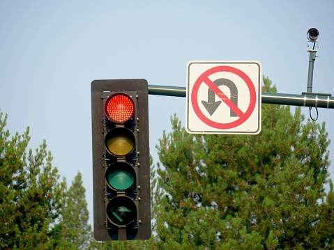 Close up of traffic lights and a no u-turn sign with treetops in the background