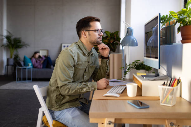 istock Side view of a young Caucasian man working from home using a desktop pc 1369401079