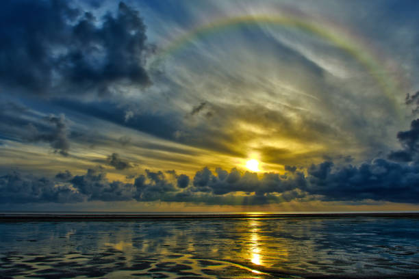 Rainbow over mud flat at low tide feahther clouds cumulus sunrise Sylt Germany