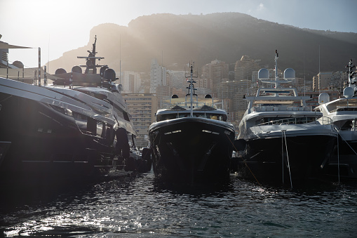 A lot of huge yachts in port of Monaco at sunset, mountain is on background, glossy board of the motor boat, megayachts are moored in marina, sun reflection on glossy board, backlight. High quality photo