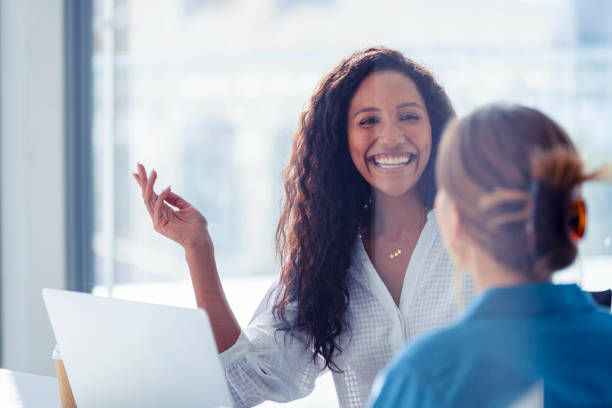 Business colleagues having a conversation Business colleagues having a conversation. They are both young business people casually dressed in a modern office. Could be an interview or consultant working with a client. She is listening and smiling. One person has her back to us. Mixed ethnic group. One is African American and the other is Caucasian customer stock pictures, royalty-free photos & images