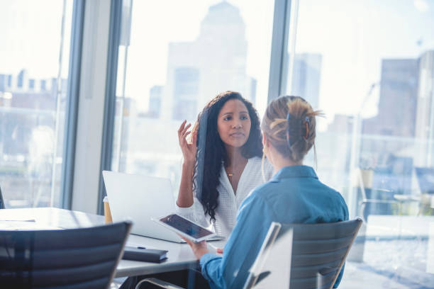 Business colleagues having a conversation. Business colleagues having a conversation. They are both young business people casually dressed in a modern office. Could be an interview or consultant working with a client. One woman looks upset, she could be getting fired. One person has her back to us. Mixed ethnic group. One is African American and the other is Caucasian fired employee stock pictures, royalty-free photos & images