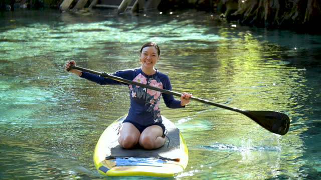 Thai woman on paddle board on river, smiling at camera