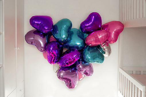 Air foil balloons hang on the wall in a heart-shaped room on Valentine's Day. Festive decoration of the apartment.