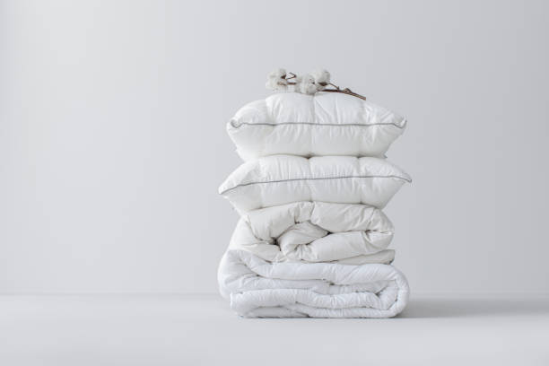 istock Folded White Linen and Pillows with a small flower branch on top, Isolated on a Grey Background 1369415826