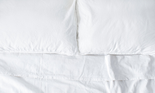 A close up shot of a neatly made bed with white sheets in a hotel room.