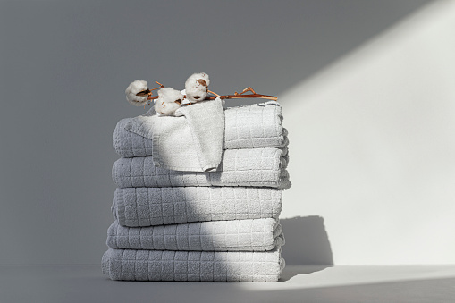 Neatly folded white hotel towels in sunlight, with a flower branch on top of them.