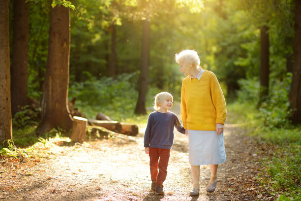 Elderly grandmother and her little grandchild walking together in sunny summer park. Grandma and grandson. stock photo