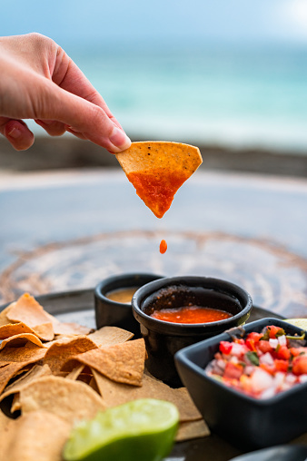 Close-up of a female's hand holding nachos with traditional red salsa