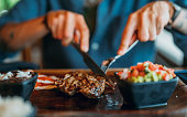 Men's  hands holding knife and fork, cutting grilled steak.