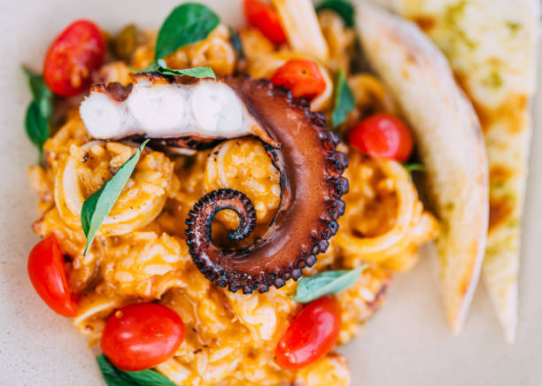 Close-up of risotto with seafood. Grilled octopus on the top decorated with cherry tomato and basil