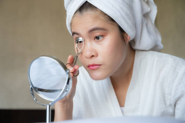 istock Young Asian woman looking mirror while using eyelash curler. 1369454209