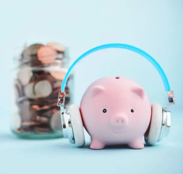 Cute pink piggy bank wearing headphones while guarding a jar full of savings. Finance, investment and savings concept