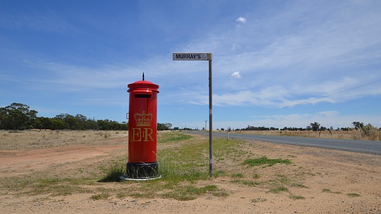 Australian outback road on hot day with deserted British red style ER post or mail box in desert