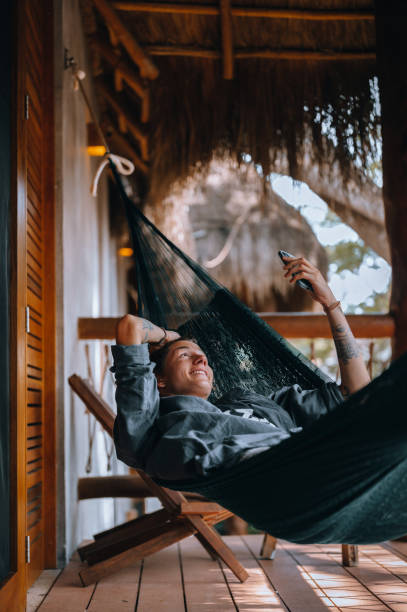 a young handsome man in a hammock makes a video call using a smartphone - telephone cabin imagens e fotografias de stock
