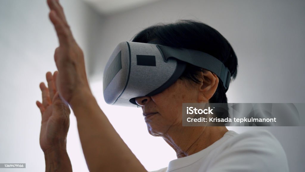 The Metaverse : Learning and using innovation Asian senior woman using VR making hand interaction  at home. 60-69 Years Stock Photo