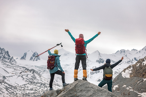 Three happy female hikers are standing with open arms in mountains and looks at glacier