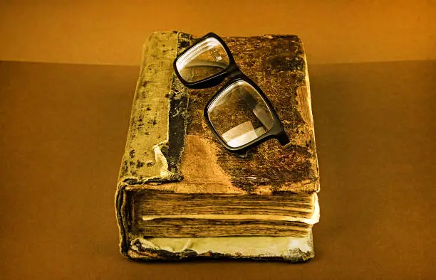 Toned Photo of the Vintage Book with a Glasses on the Brown Background closeup