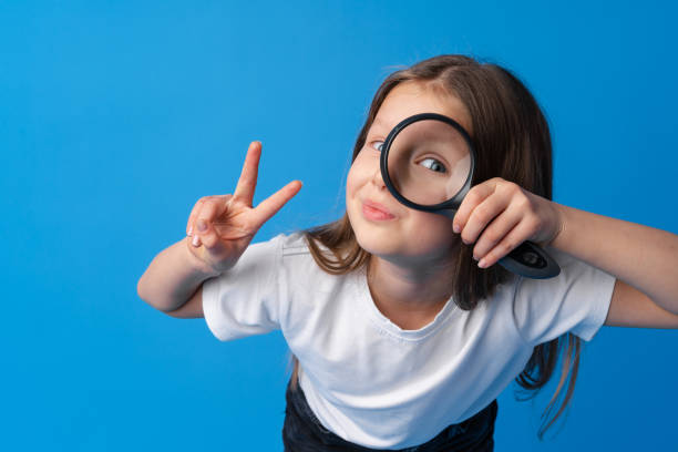 istock Little girl looking through a magnifying glass on blue background 1369489801