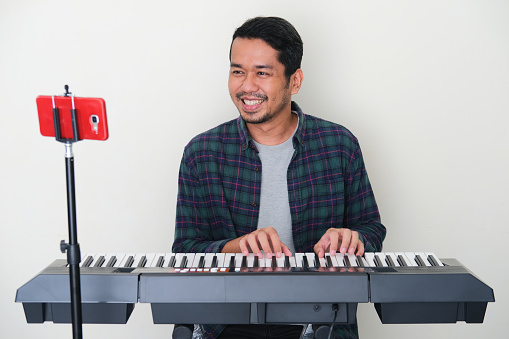 Adult Asian man smiling happy when learning playing piano on online course