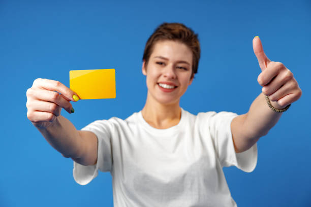 imagen de una mujer joven sosteniendo una tarjeta de visita con espacio de copia sobre fondo azul - invitation blank smiling business card fotografías e imágenes de stock