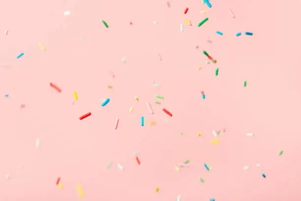 Photo of flying colorful sprinkles over pink background