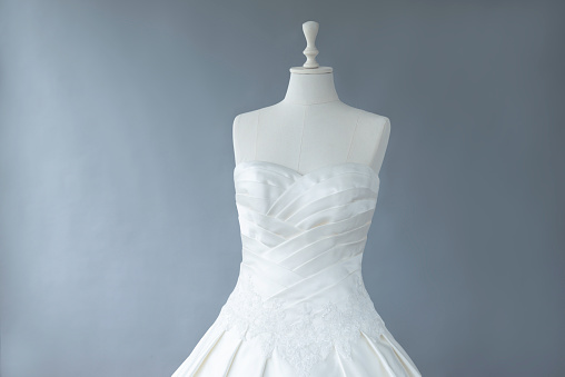 Wedding dress on tailor mannequin in front of gray wall.