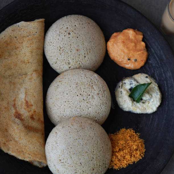 Jowar or sorghum idli and dosa with chutneys South India snacks idli and dosa made with rice, black gram or urad dal and jowar or sorghum. Healthy snack with a twist. Served on black place with white coconut chutney, red tomato chutney and orange malgapodi or milagai podi or gun powder chutney. thosai stock pictures, royalty-free photos & images