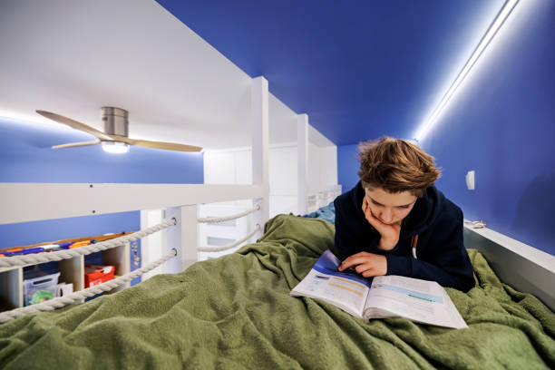 istock Teenage boy lying in bed and studying for school 1369497199