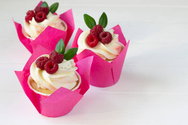 istock Cupcakes  decorated with fresh raspberry  , white wooden board.  Baking background, cake design, cake decoration, Fruits cup cakes, menu design or recipe background 1369498612