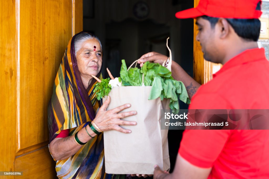 focus on senior women, Indian delivery boy giving groceries to senior women after opening door - concept of online order service and e-commerce transportation. focus on senior women, Indian delivery boy giving groceries to senior women after opening door - concept of online order service and e-commerce transportation India Stock Photo