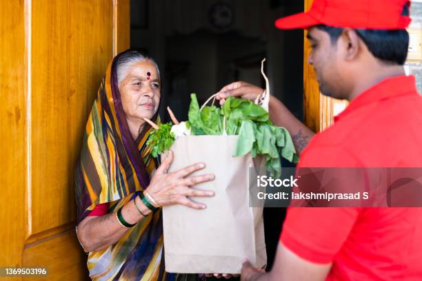 Focus On Senior Women Indian Delivery Boy Giving Groceries To Senior Women After Opening Door Concept Of Online Order Service And Ecommerce Transportation Stock Photo - Download Image Now