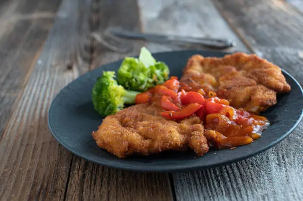 Breaded pork schnitzel with spicy
Puszta sauce cooked with bell peppers, onions and tomatoes. Served on a plate with broccoli isolated on wooden table with copy space