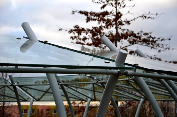 fahrradabstellraum mit glasdach mit gepunktetem aufdruck. konstruktion aus gebogenen grauen rohren in einen lichtbogen. gehärtetes verbundglas, das an metallgriffen in einem stadtpark befestigt ist. - x stand stock-fotos und bilder